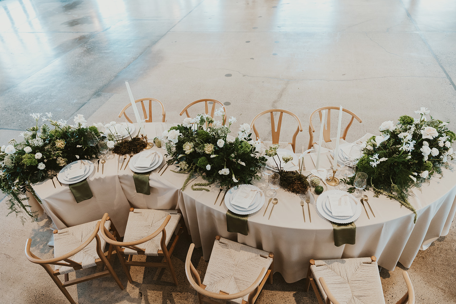 Elegant wedding reception table with lush greenery, white florals, and gold place settings