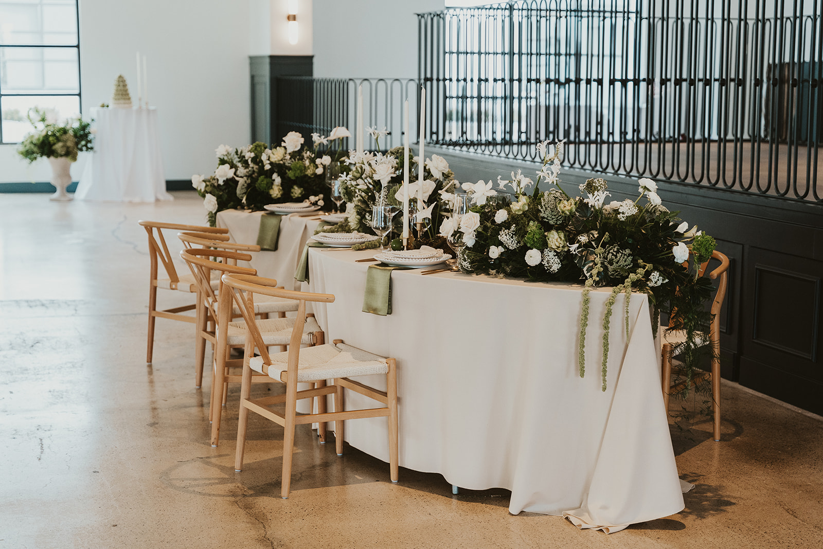 Elegant wedding reception table with white florals, greenery, and candles in a modern venue