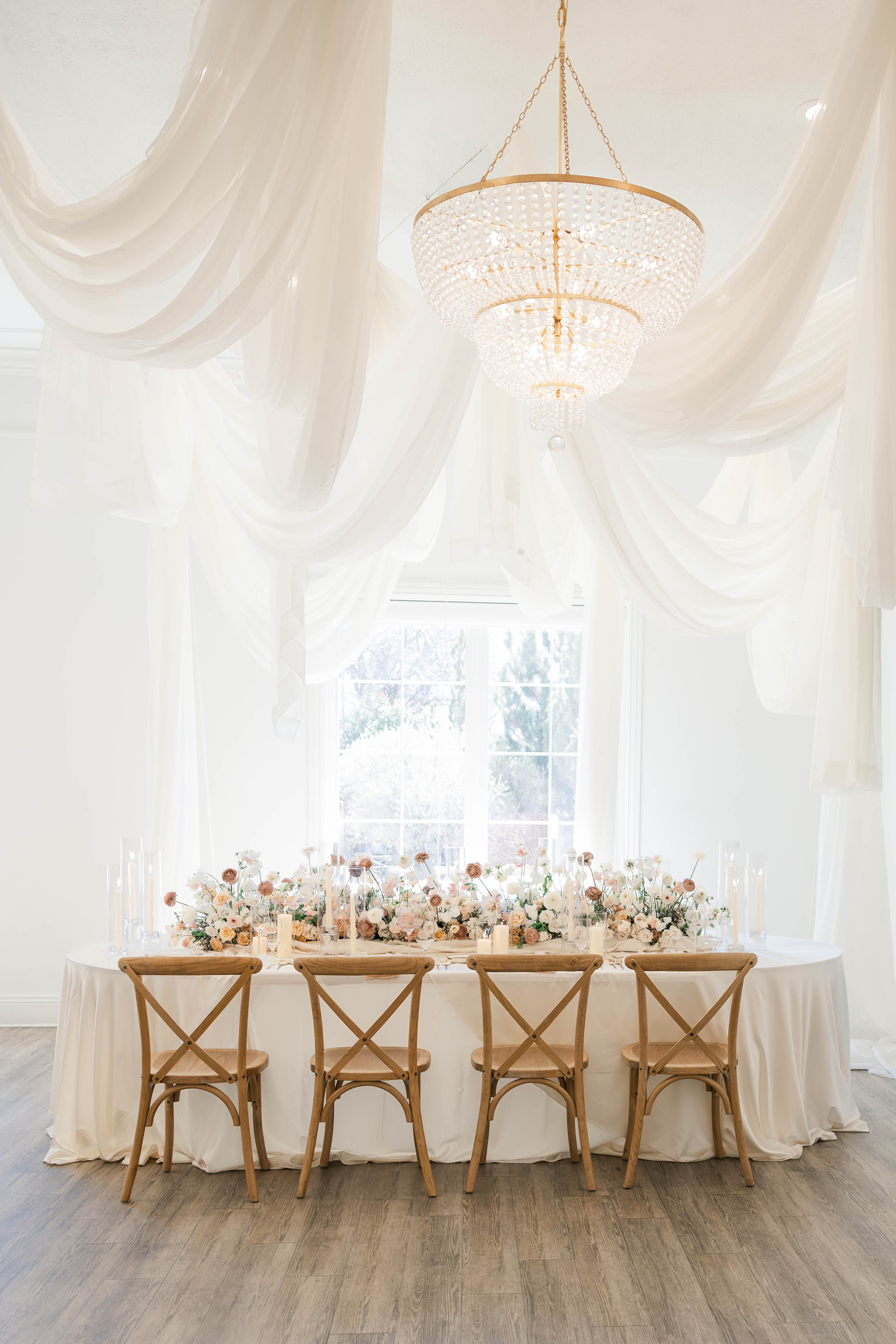 Elegant wedding reception table with chandelier, draped fabric, and lush floral centerpieces